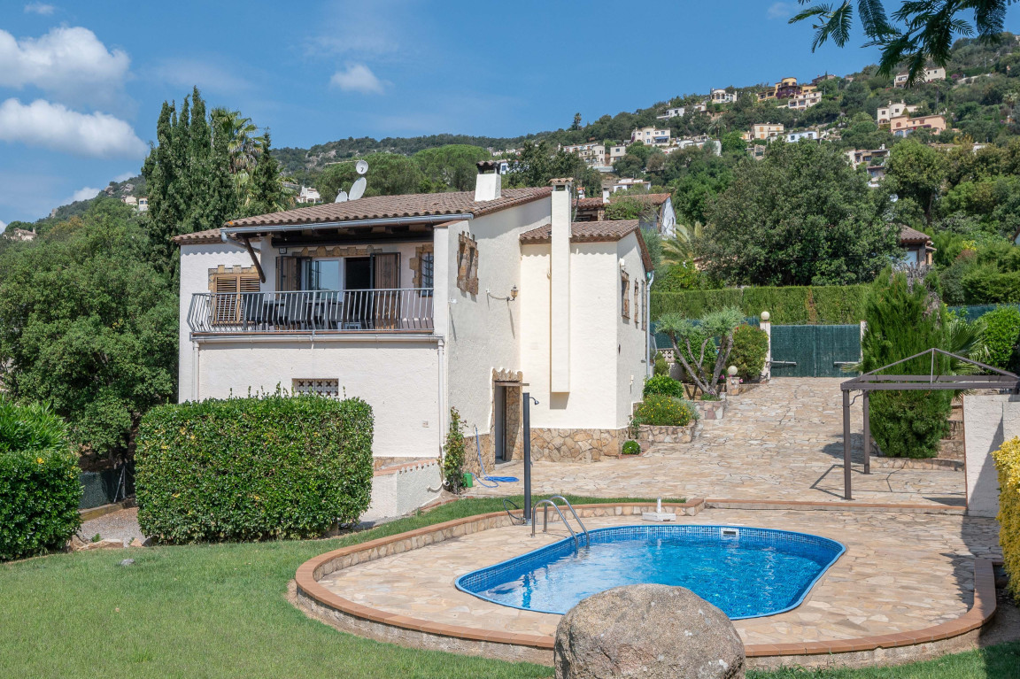 Facade with covered terrace of villa with swimming pool in Calonge. Background with other villas on mountain.